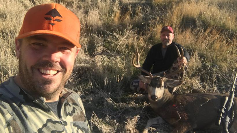 Father and son posing with harvested mule deer