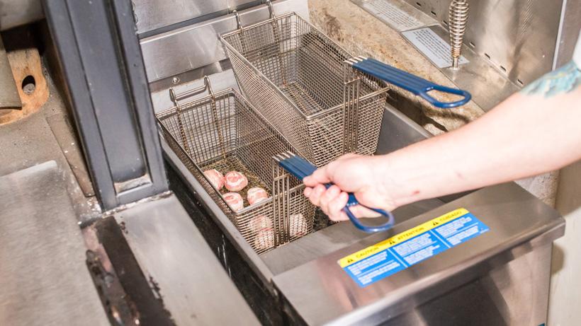 Lowering elk meatballs wrapped in bacon into fryer